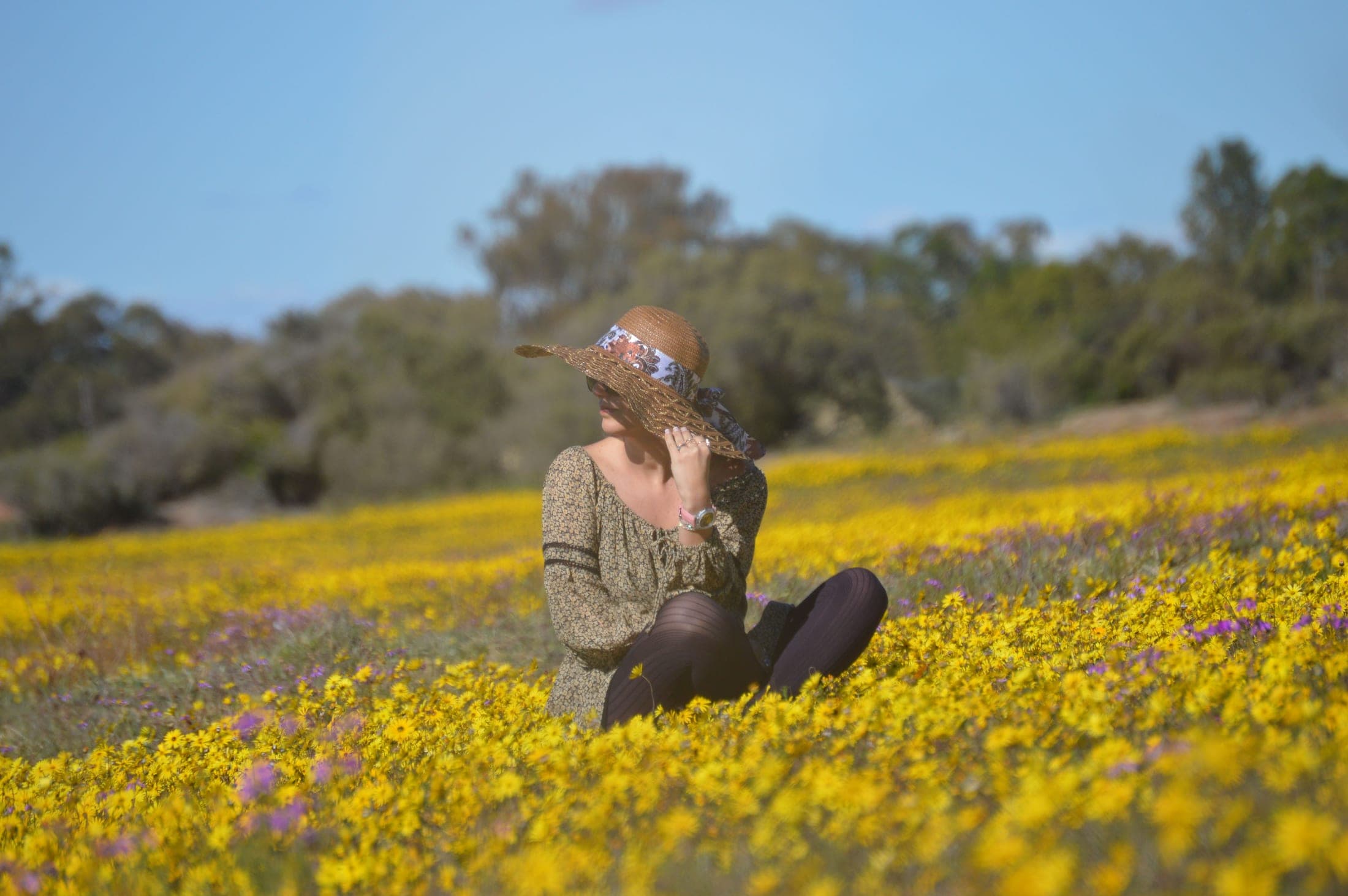 A woman sitting in a field of yellow and purple wildflowers, wearing a Livia Karsten watch
