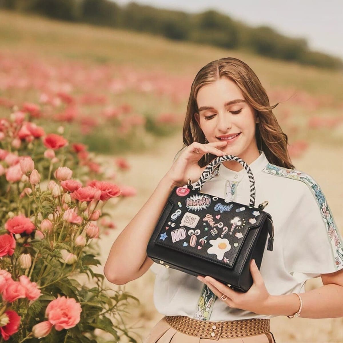 A model holding a patch bag in a field of pink poppies