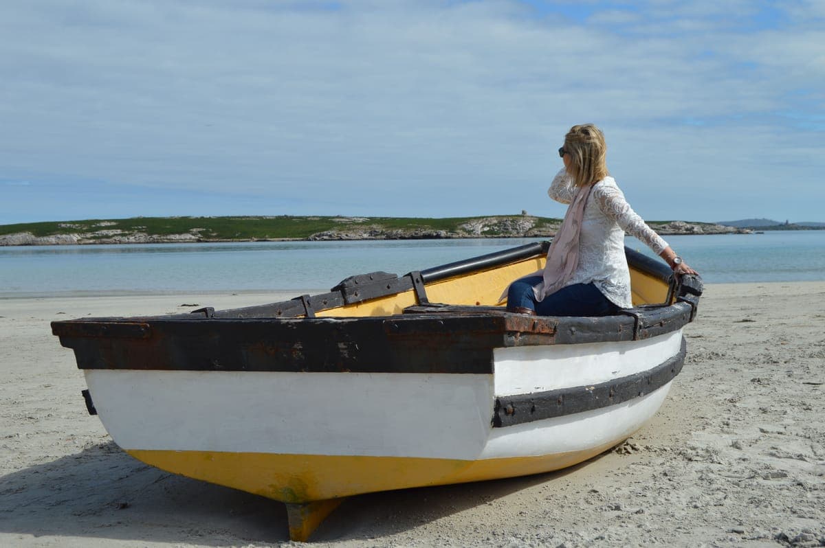 A woman sitting on a wooden boat pulled up on a beach